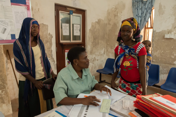 health worker with papers in clinic in Tanzania with two young women